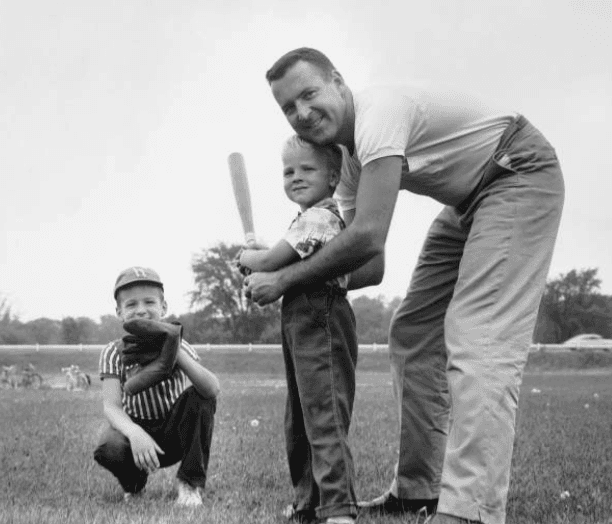 Black-and-white scene of boys playing sandlot baseball in a 1950s neighborhood