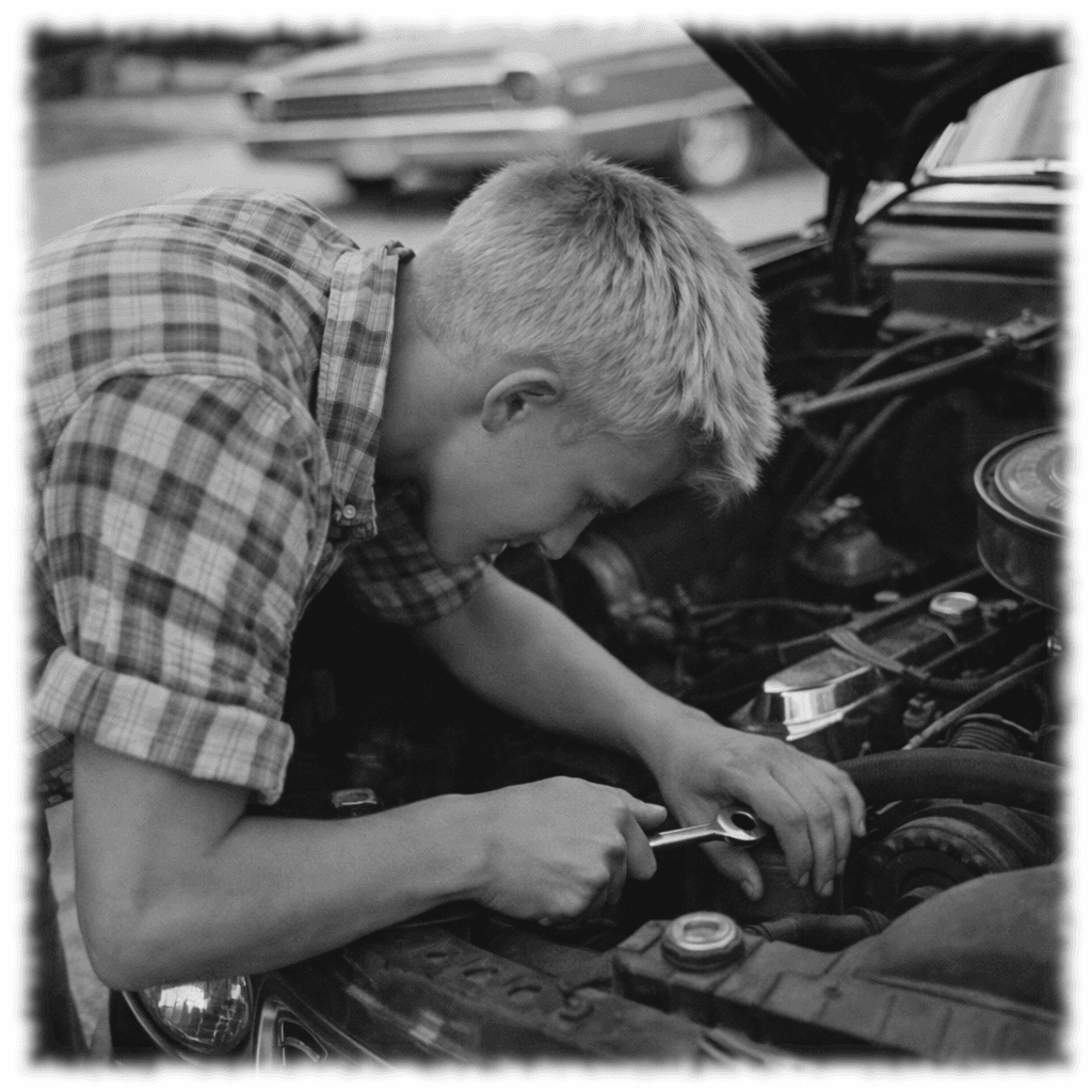 Black-and-white photo of a young man working on a car engine in a garage