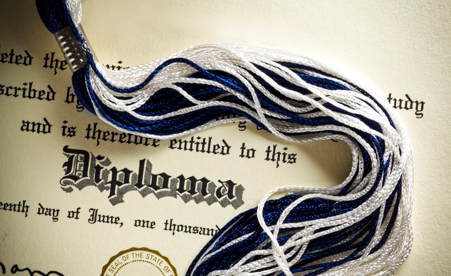 A university diploma with a blue-and-white graduation tassel laid across it